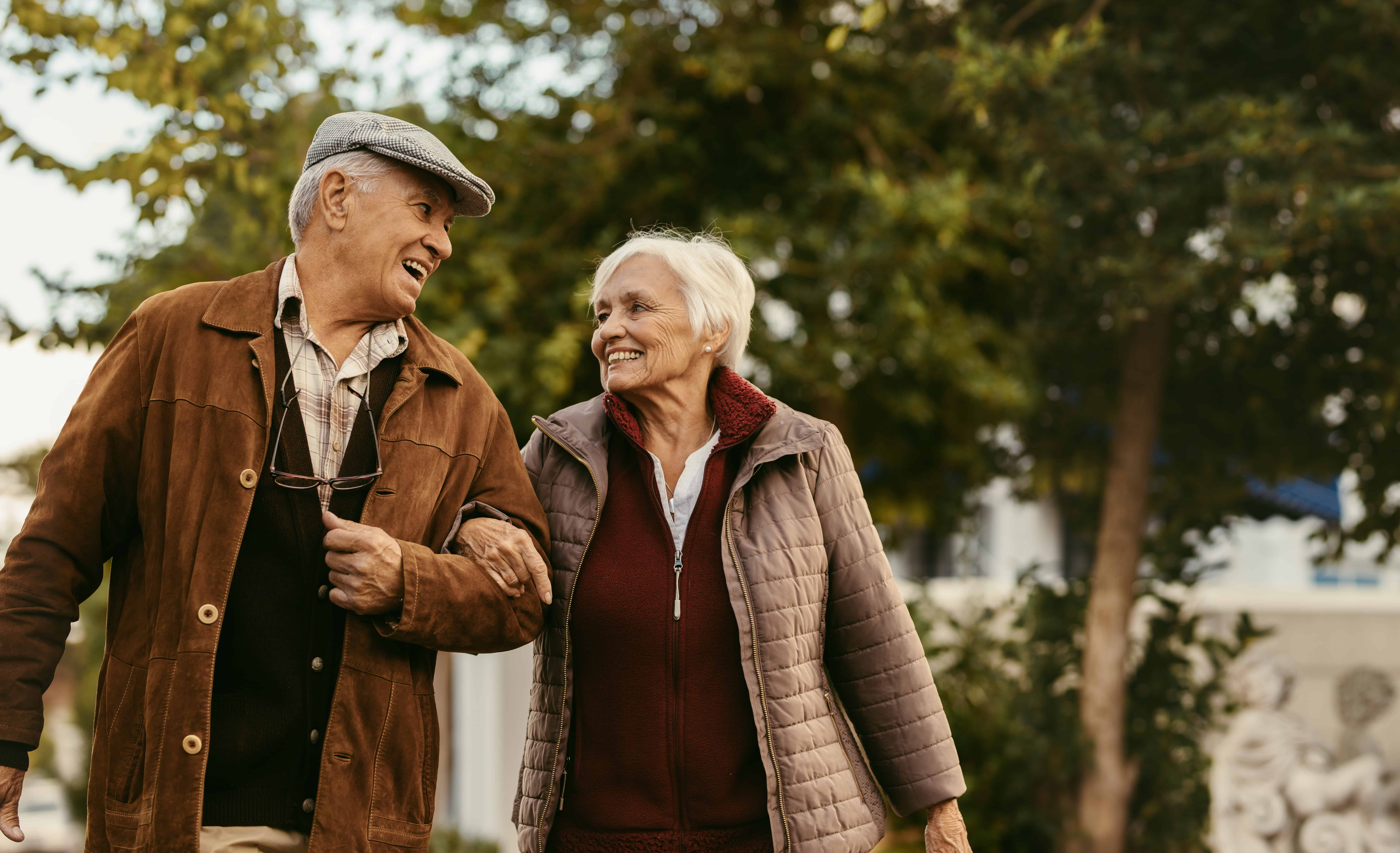 an elderly couple lock arms on their walk in the park