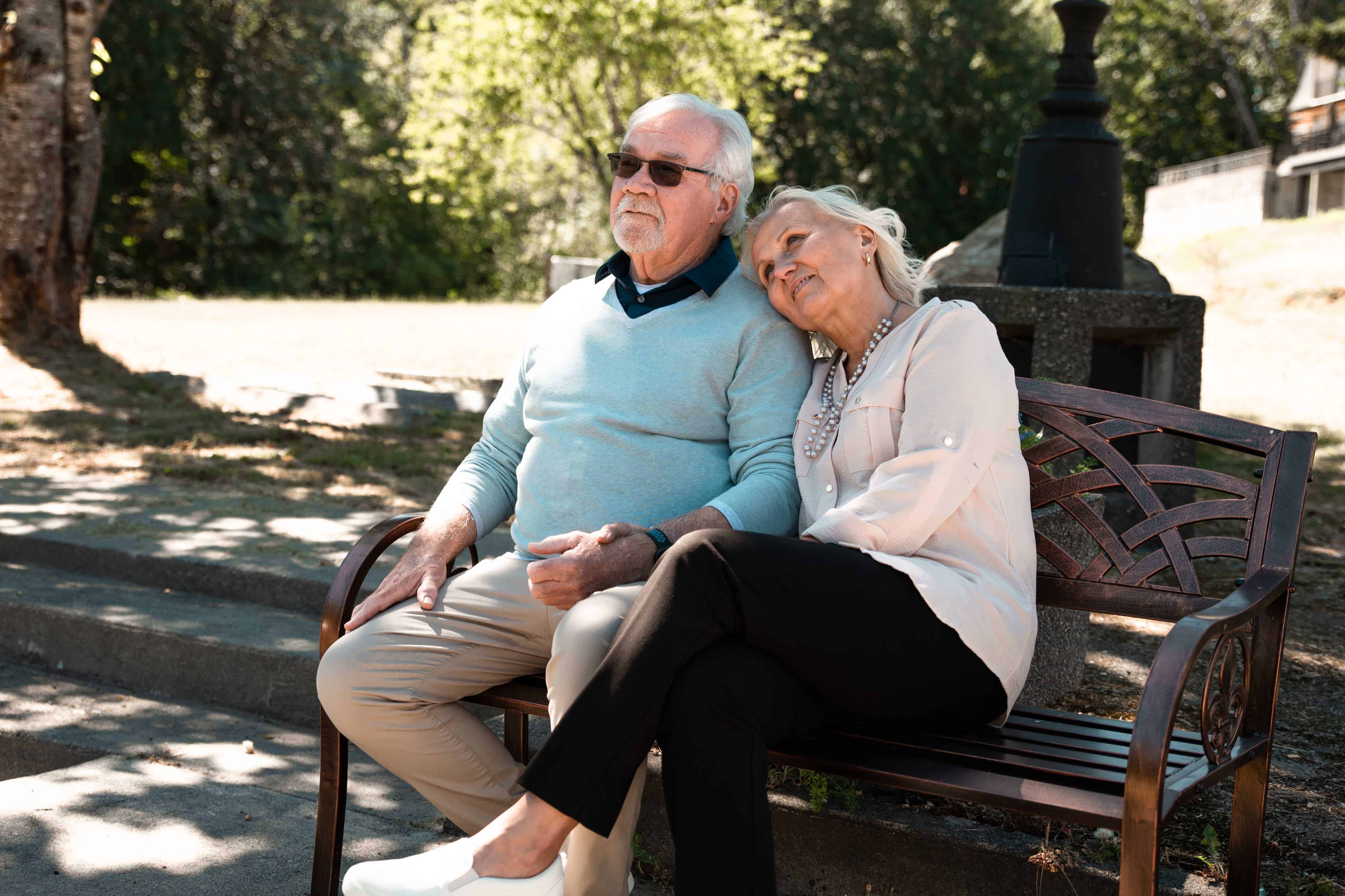 a senior couple sit on a bench together outside and look on
