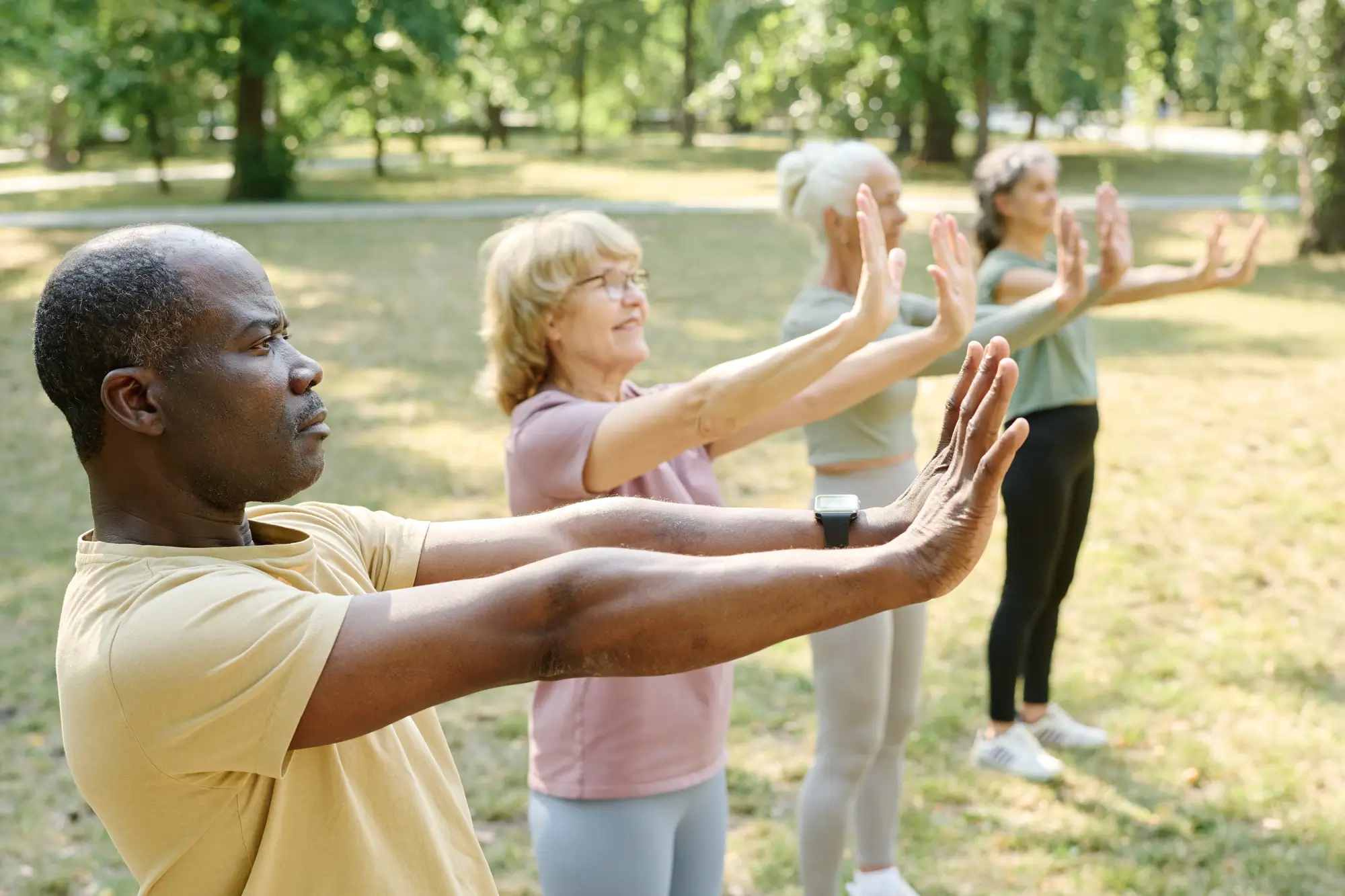 diverse group of 4 seniors doing tai chi together in sunny park