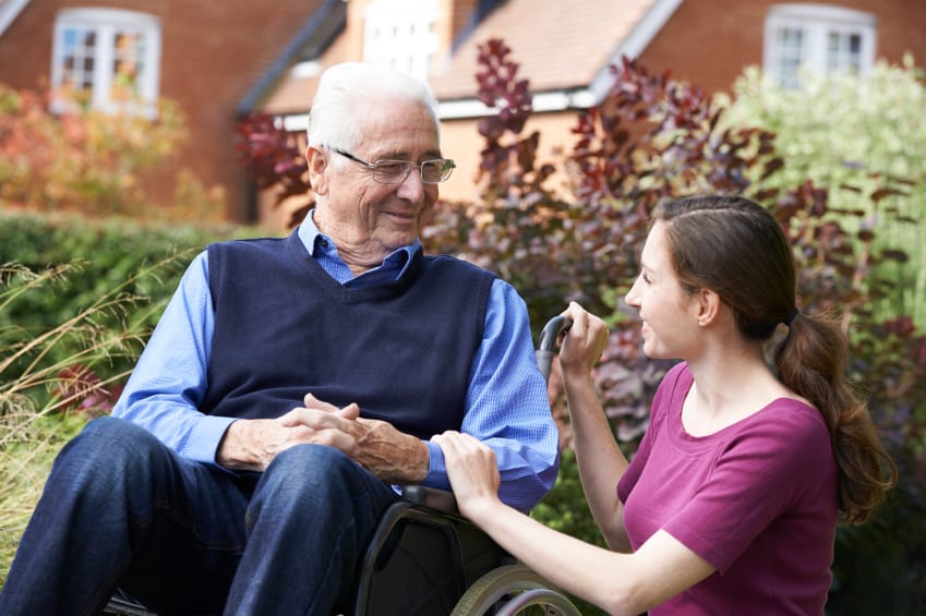 caregiver comforts a senior man who sits on his wheelchair
