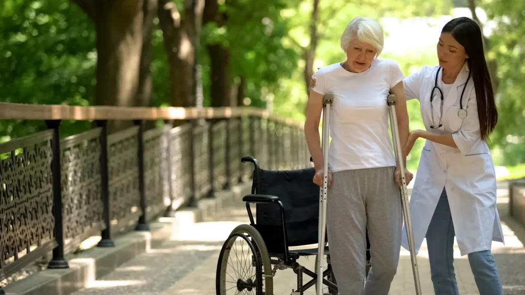 doctor helping mature woman walk down sidewalk with crutches
