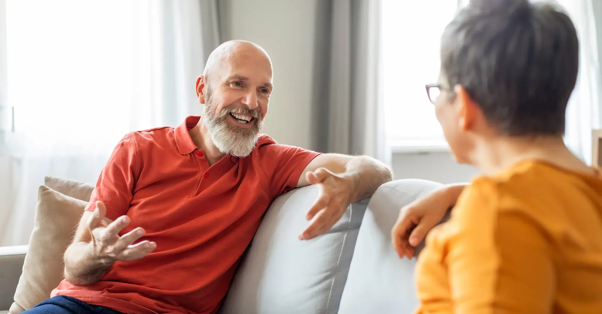 smiling man sits on couch with older woman while they have a conversation
