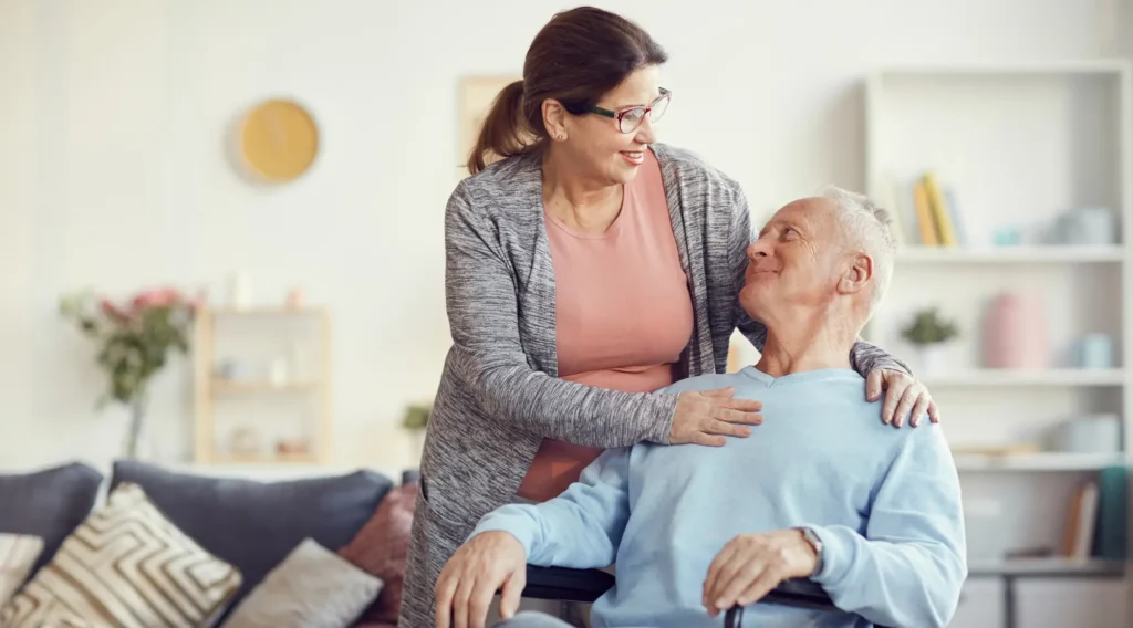 woman has hand on chest of her husband in wheelchair in their living room