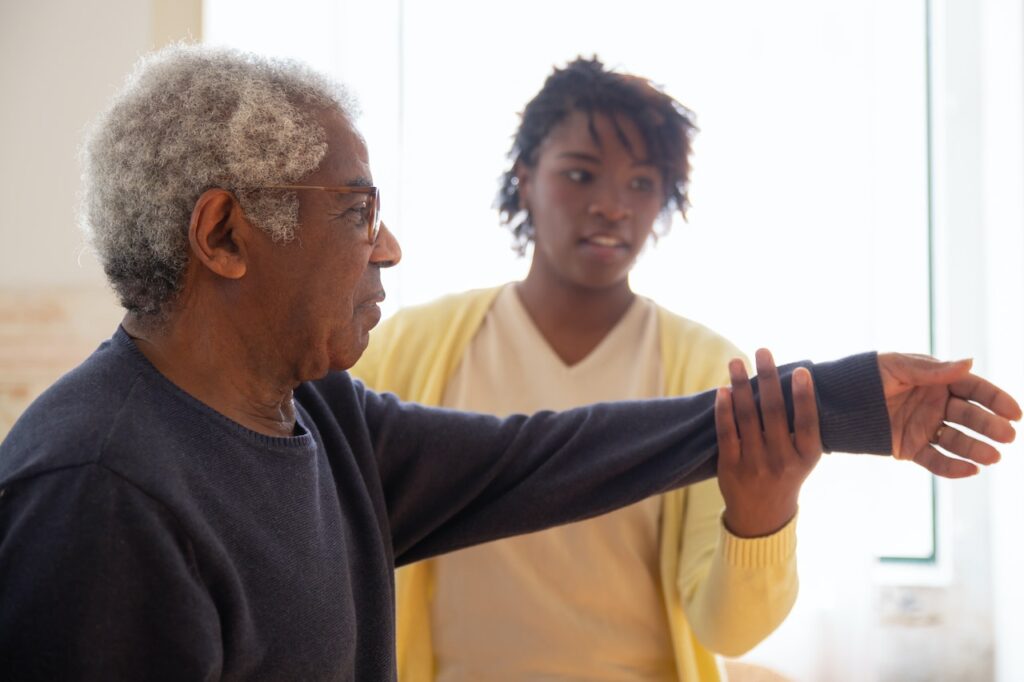 an in-home caregiver supports an elderly man with his home exercises