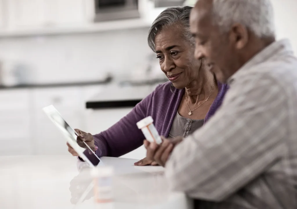 mature couple sitting at kitchen table reviewing documents, the man holds a pill bottle