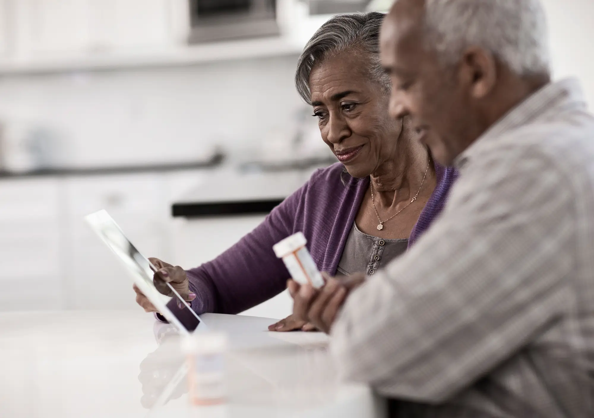 mature couple sitting at kitchen table reviewing documents, the man holds a pill bottle
