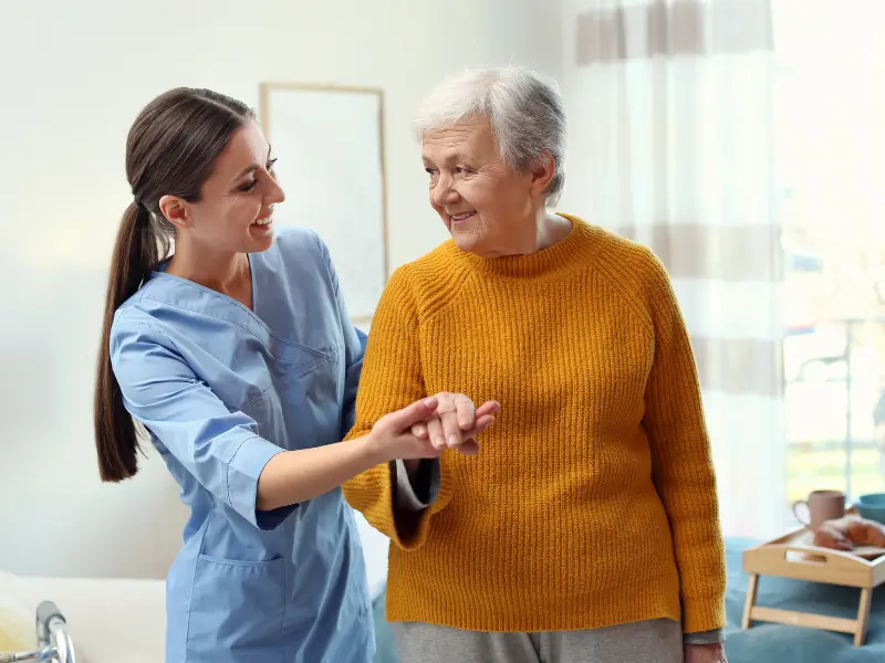 a caregiver supports an elderly woman walk in their home