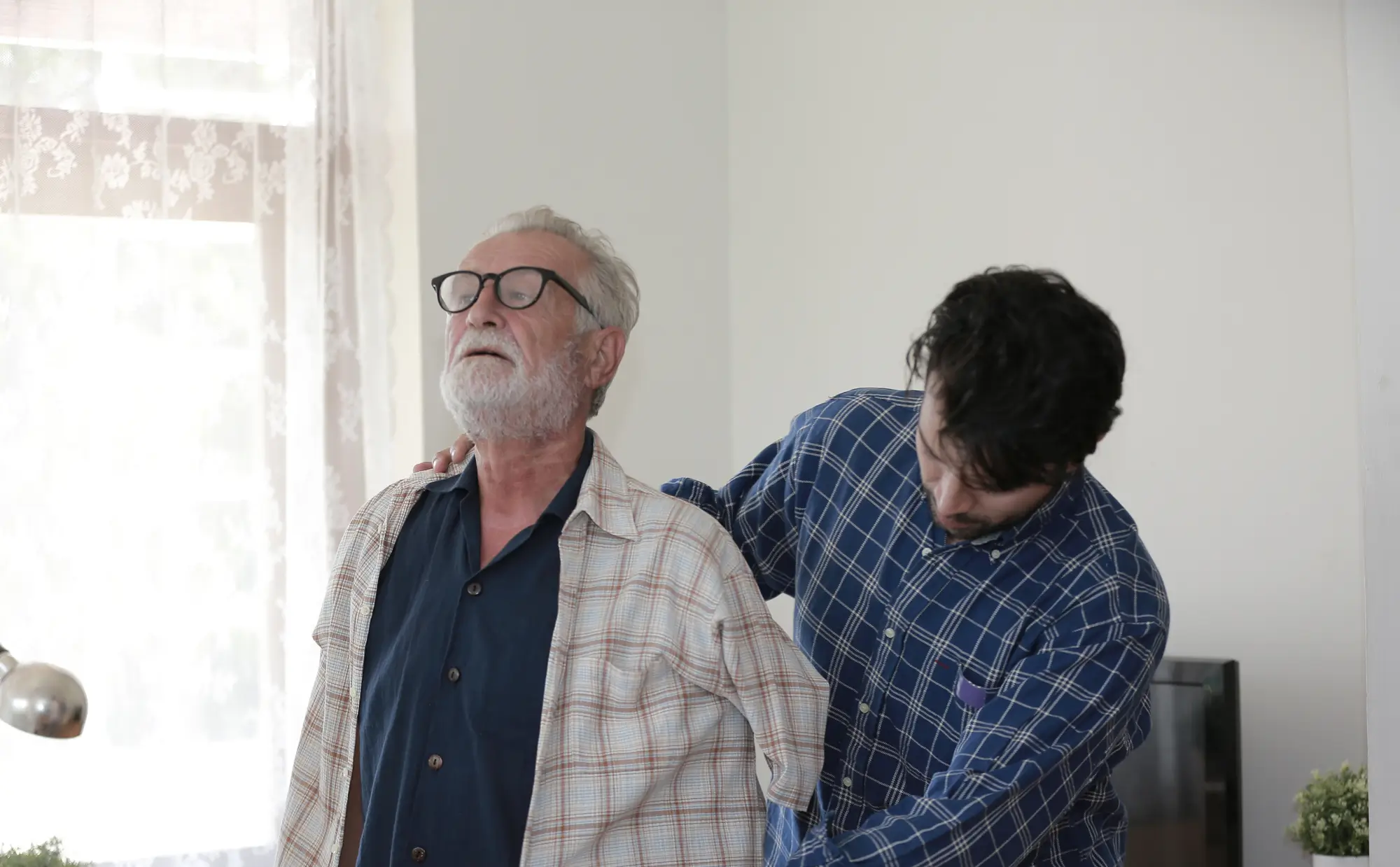 helping senior man put on overshirt at home