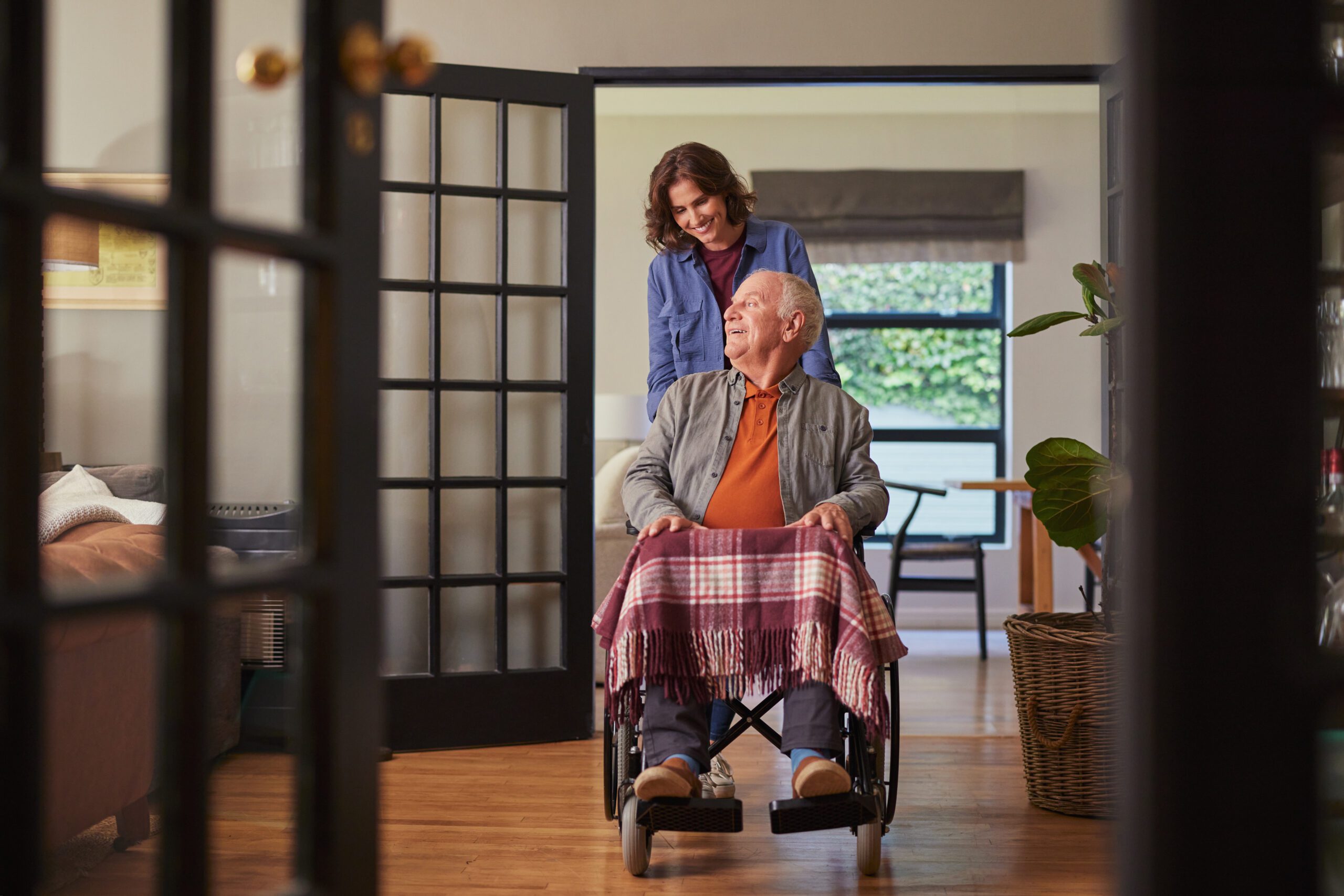 Senior man in wheelchair pushed by smiling woman