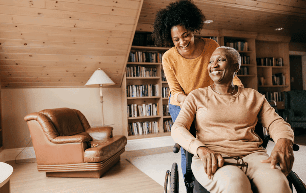 young woman pushes older woman in wheelchair in home library