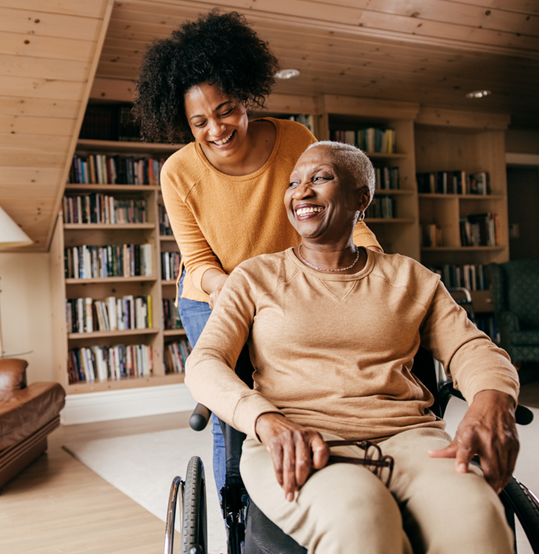 young woman pushes older woman in wheelchair in home library