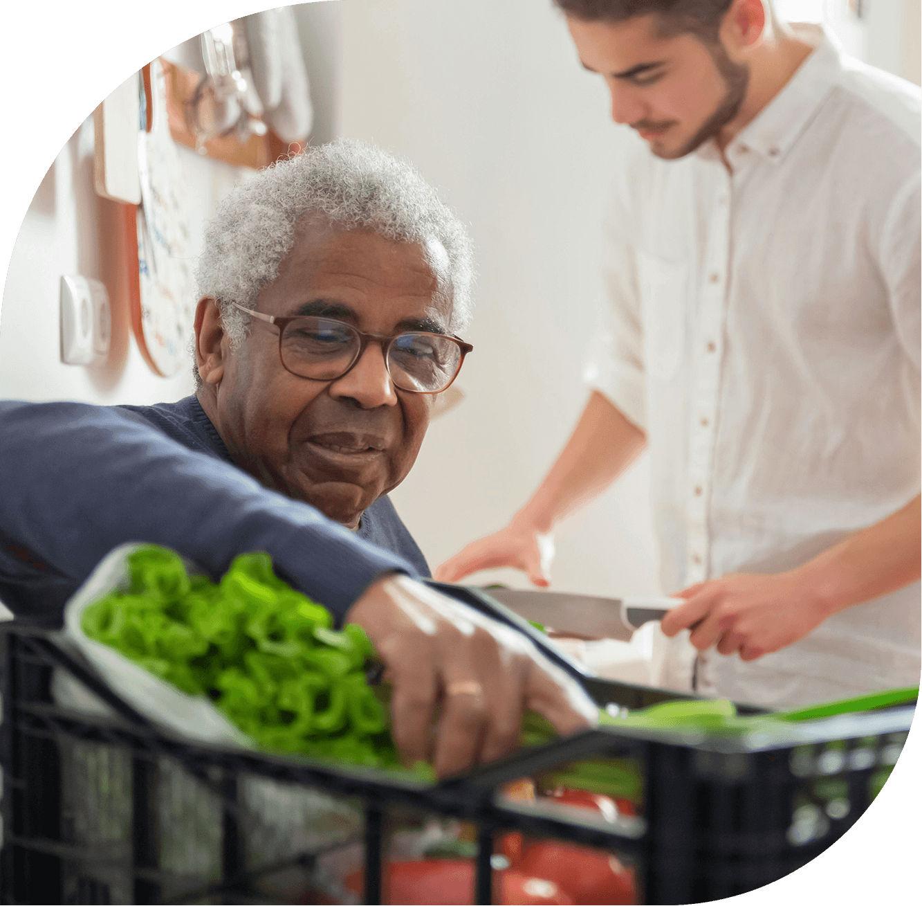 young man helps older man unpack fresh groceries from crate in home kitchen
