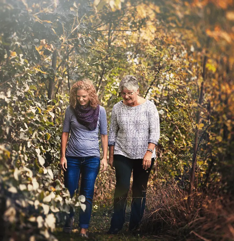 young woman and mature woman walking on a wooded trail in early autumn