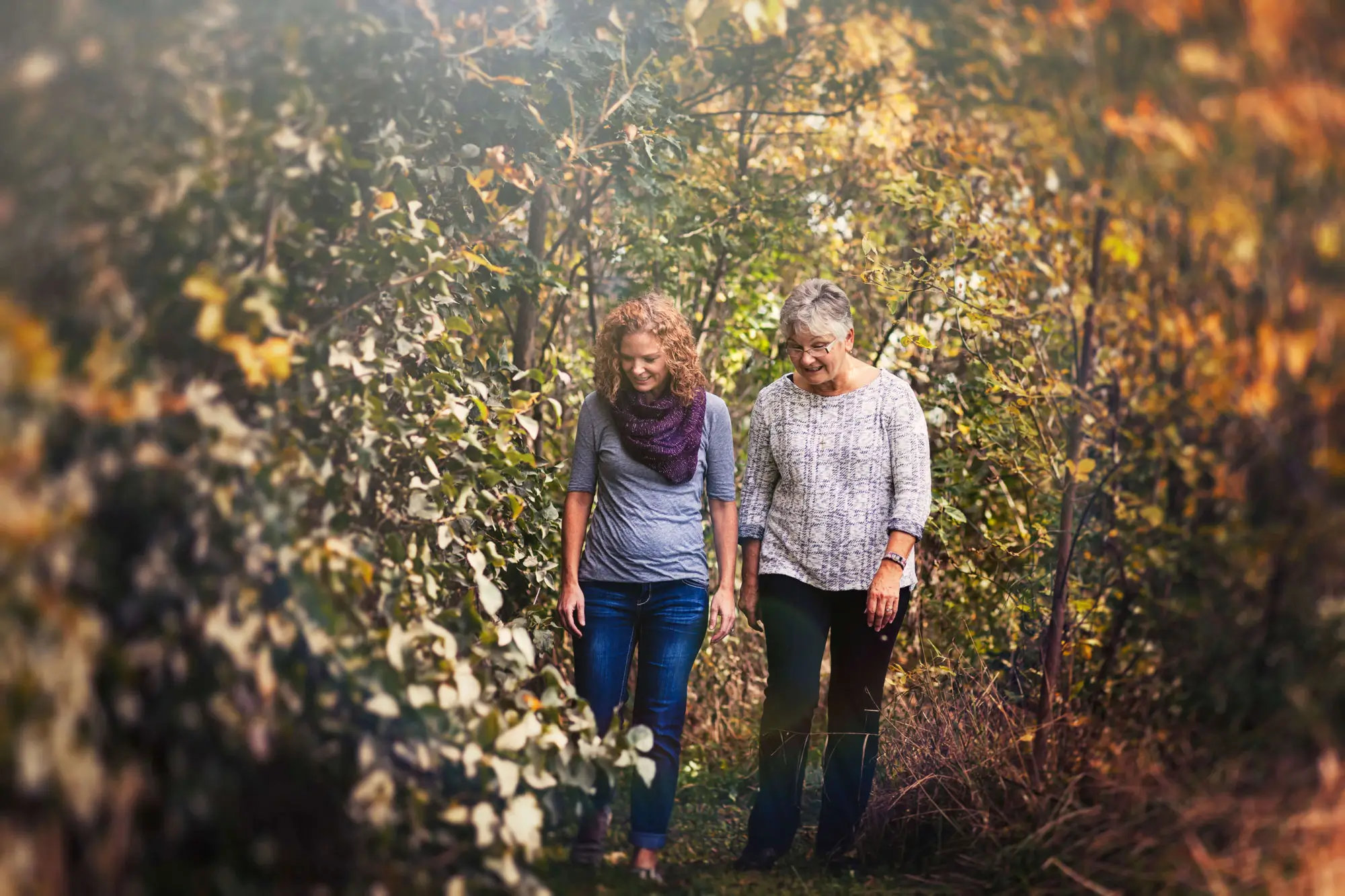young woman and mature woman walking on a wooded trail in early autumn