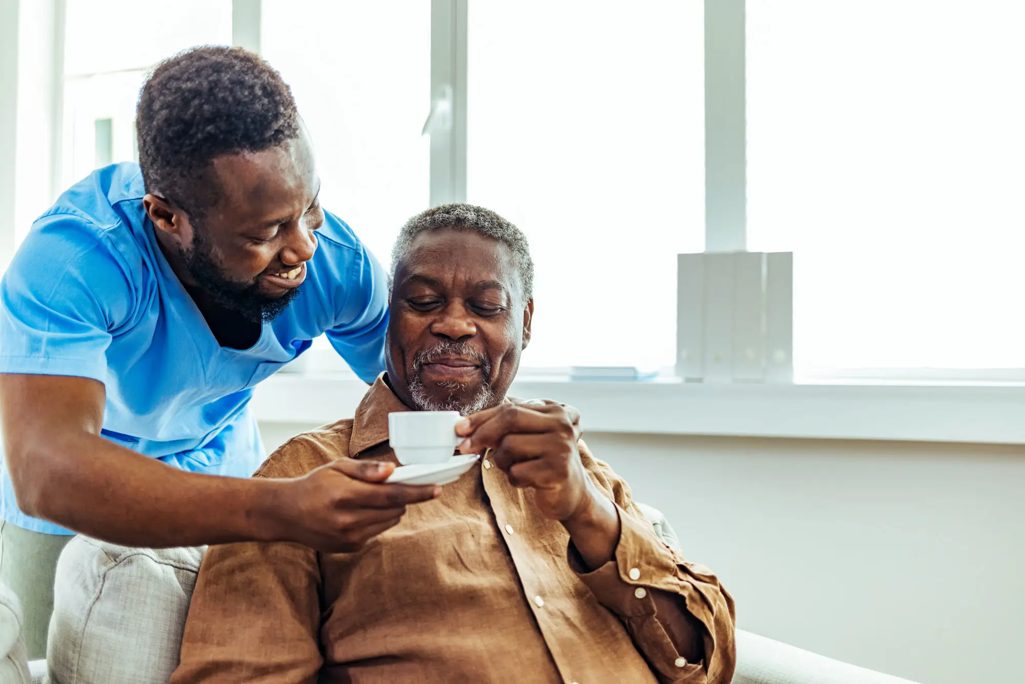 male caregiver offers senior man cup of espresso in home