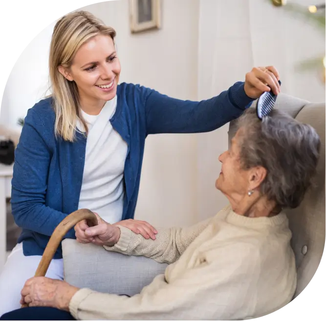home caregiver brushes senior woman's hair as she sits in armchair