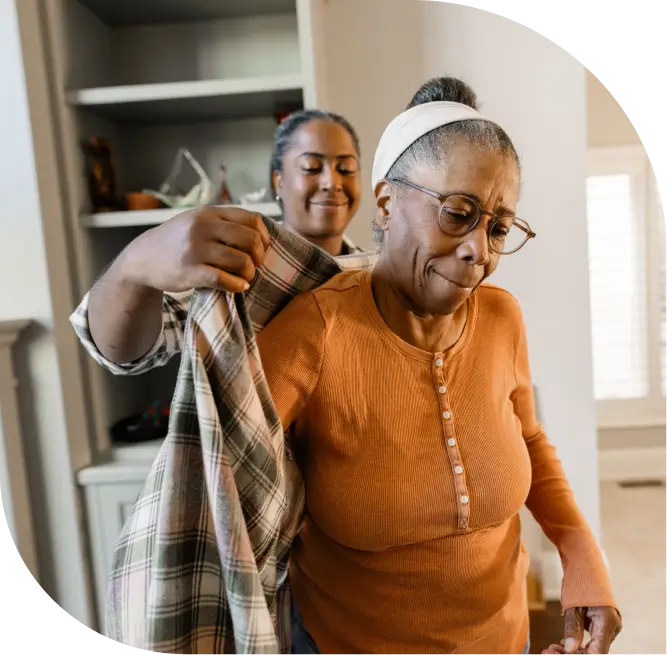 caregiver helps senior woman put on a flannel shirt