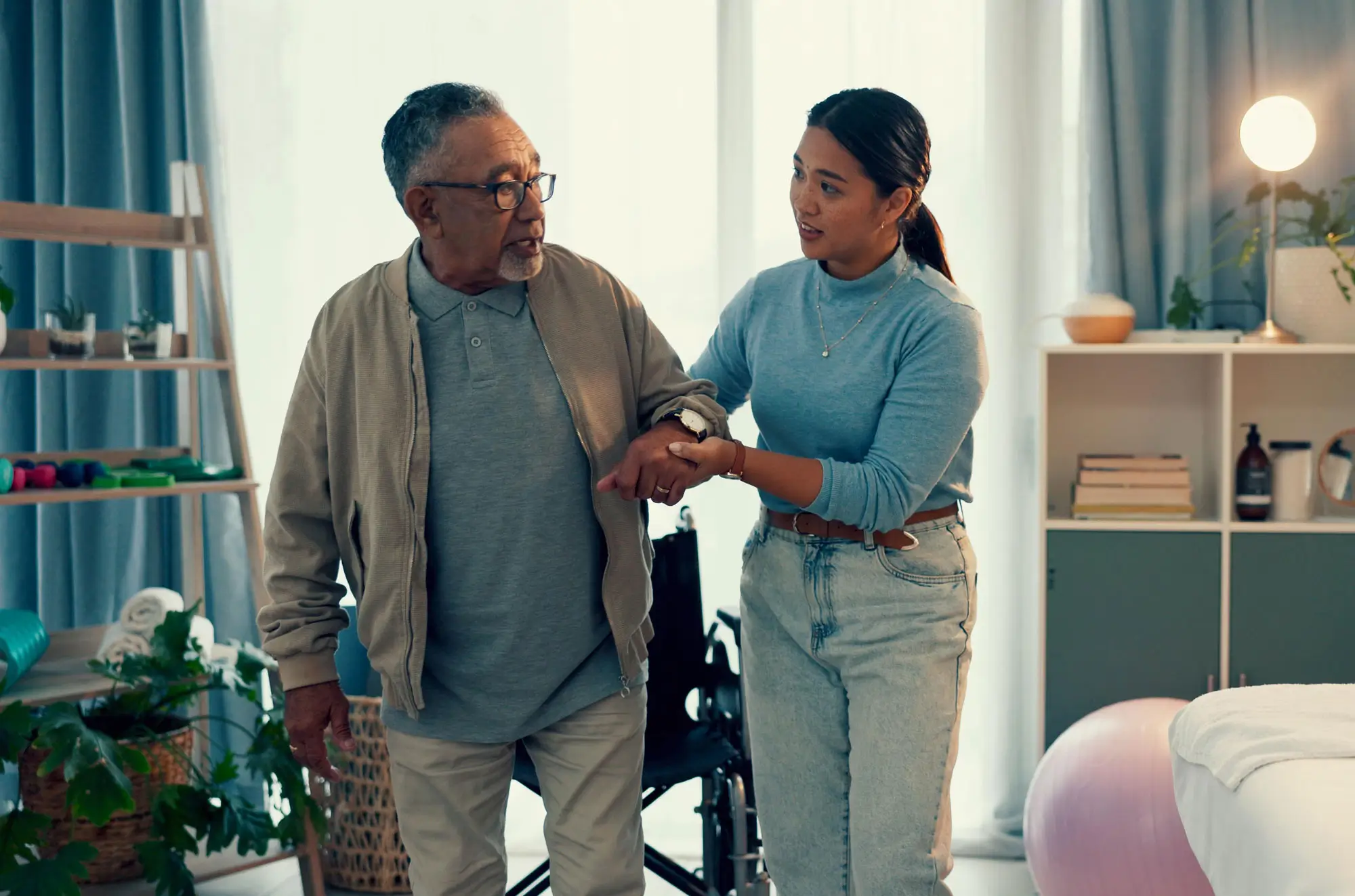 female caregiver helps senior man stand up from wheelchair